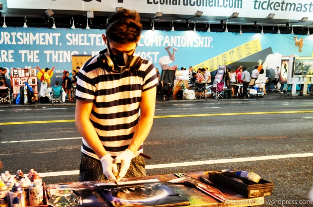 A talented artist along the sidewalk (spray) paints a different take of the NYC skyline.